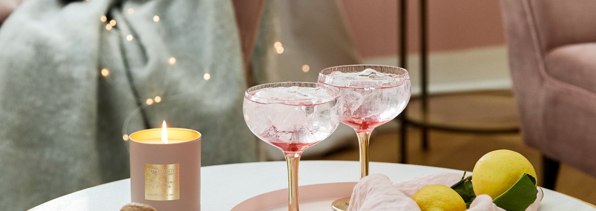 due coppe cocktail rosa con ghiaccio su tavolo aperitivo con candela e limone